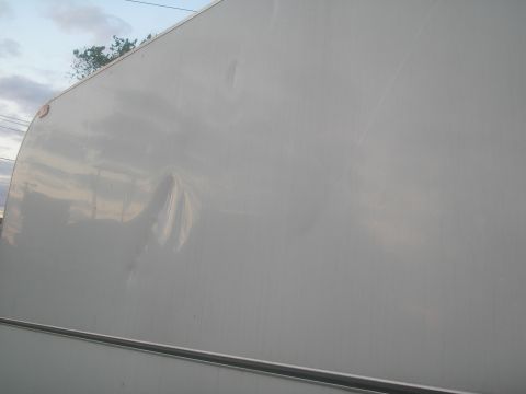 1990 Ford Bronco - Side of a white trailer shows a significant dent.