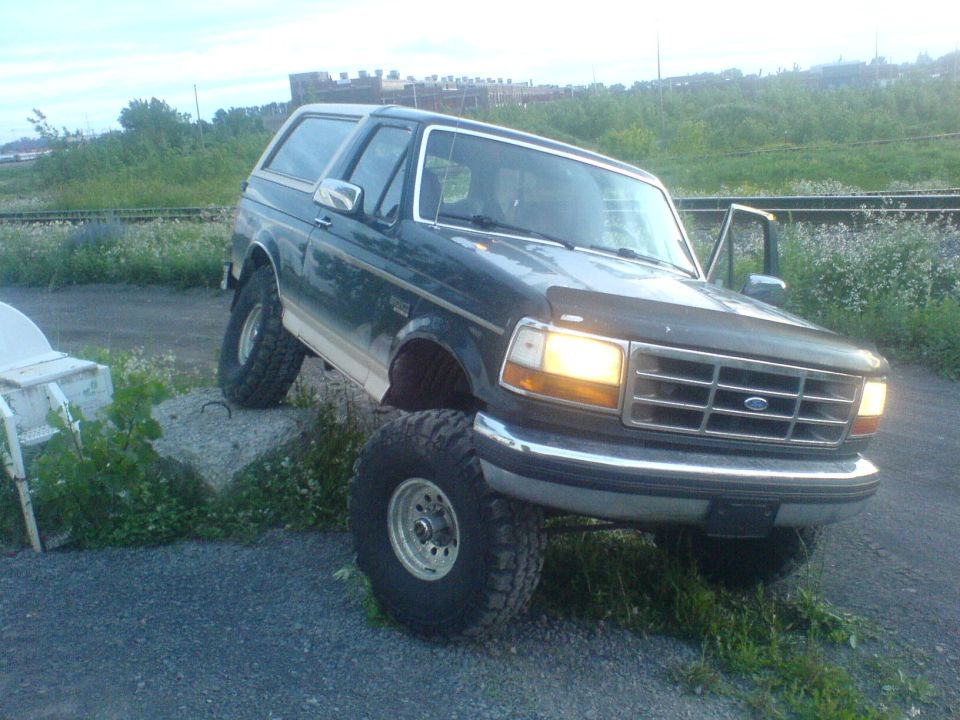 Dark green Ford Bronco with lifted suspension and large tires, parked on gravel and grass