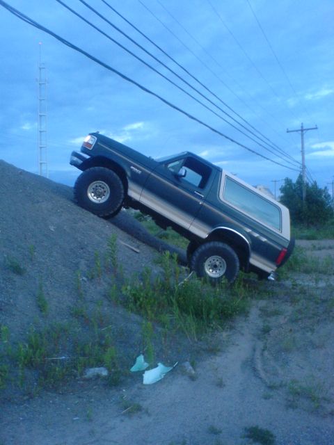 1985 Ford Bronco - This 1985 Ford Bronco is captured mid-climb on a steep dirt embankment under a cloudy sky.