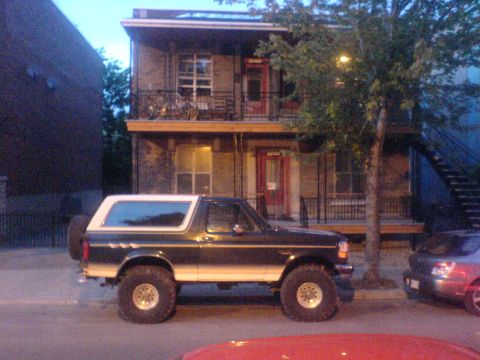 1985 Ford Bronco - This lifted Ford Bronco is parked on a street in front of a multi-story building.