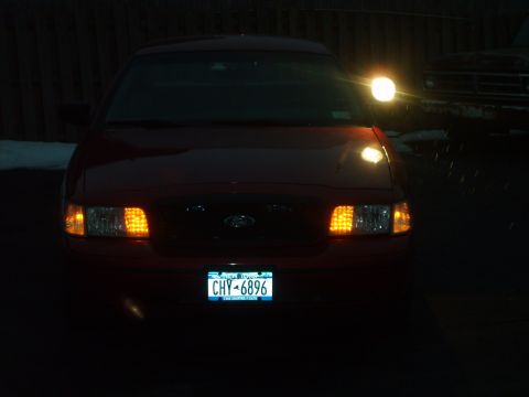 2000 Ford Crown Victoria - Front view of a red 2000 Ford Crown Victoria at night, with its headlights and turn signals illuminated.
