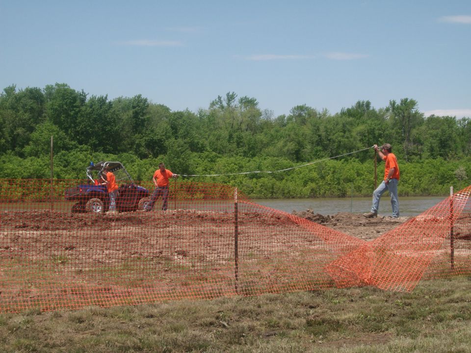 Side-by-side utility vehicle with two people near a body of water, men in orange shirts working with a tape measure