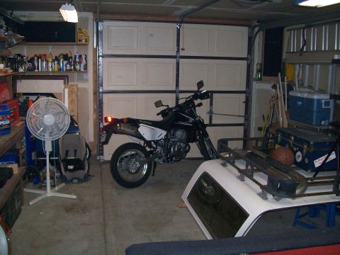 1990 Ford Bronco - A Suzuki motorcycle is parked inside a garage, with a white truck cap visible in the foreground.