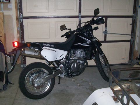 1990 Ford Bronco - A black Suzuki motorcycle is parked in a garage, with the rear tire and exhaust clearly visible.