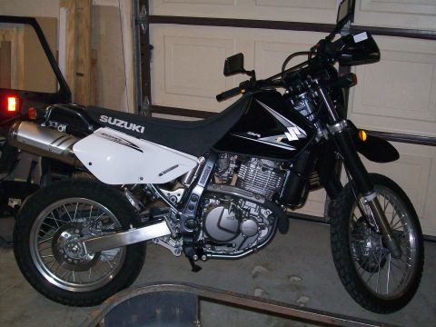 1990 Ford Bronco - A Suzuki DR-Z motorcycle is parked indoors with a garage door in the background.