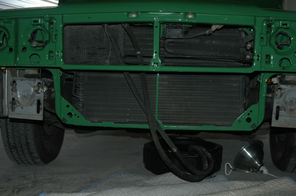 Car front end stripped to green radiator support with radiator exposed and drain pan below