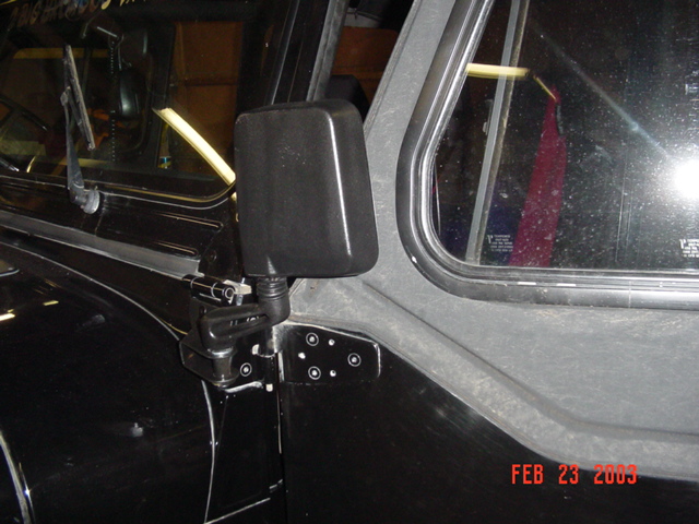 Black side-view mirror mounted on the door hinge area of a dark vehicle, shot at night