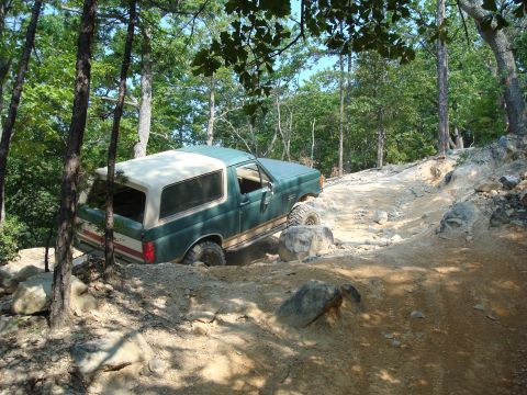 1990 Ford Bronco - A green 1990 Ford Bronco tackles a challenging, rocky trail during an off-road excursion.
