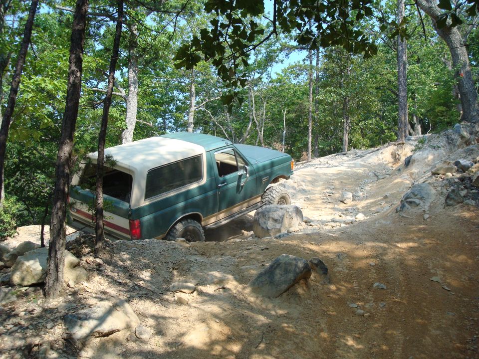 Green 1990 Ford Bronco navigating a rocky off-road trail