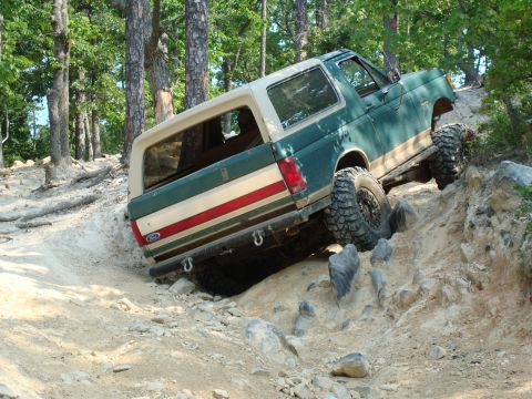 1990 Ford Bronco - Ford Bronco navigating a challenging off-road trail with large rocks and steep inclines.