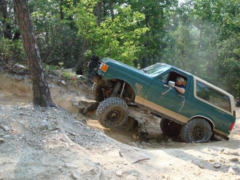 1990 Ford Bronco - A green Ford Bronco navigates a challenging rocky off-road trail.