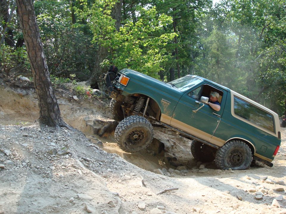 Green Ford Bronco with tan trim climbing a rocky incline, driver visible