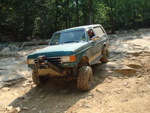 1990 Ford Bronco - A green Ford Bronco navigates a challenging rocky terrain on an off-road trail.