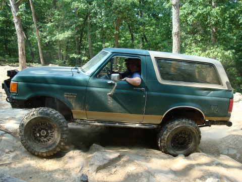 1990 Ford Bronco - This 1990 Ford Bronco is shown off-roading on a rocky trail with trees in the background.