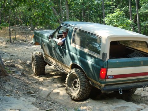 1990 Ford Bronco - This Ford Bronco is navigating a challenging off-road course with large rocks and trees.
