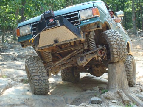 1990 Ford Bronco - A green Ford Bronco navigates a rocky off-road course, with one tire resting on a log.