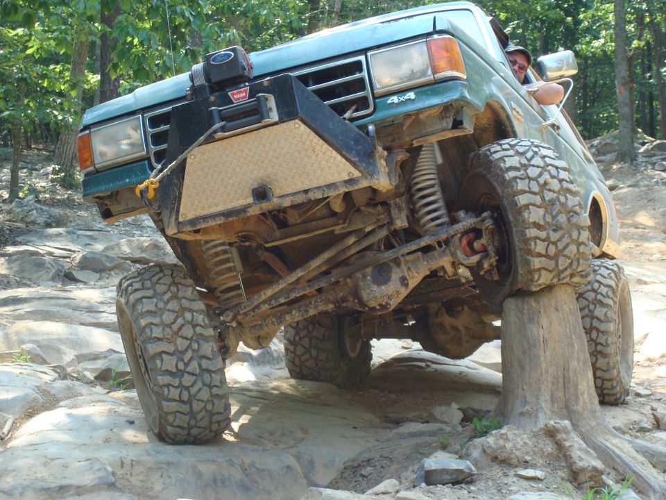 Green Ford Bronco with a winch on the front bumper, tires on rocks and a log