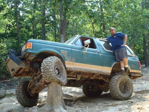 1990 Ford Bronco - A man poses with a lifted green 1990 Ford Bronco during an off-road excursion.
