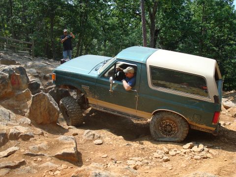 1990 Ford Bronco - Ford Bronco tackling a challenging rocky trail with a driver and passenger visible.