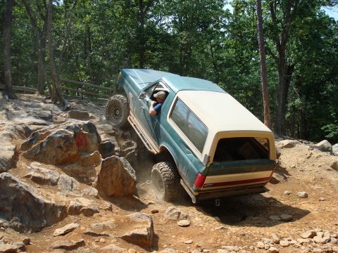 1990 Ford Bronco - A Ford Bronco navigates a challenging off-road trail with steep rock formations.