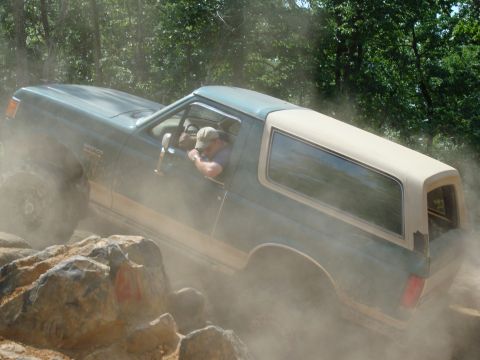 1990 Ford Bronco - A 1990 Ford Bronco is shown off-roading through dust and rocks.