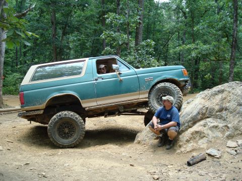 1990 Ford Bronco - A man watches as a lifted Ford Bronco navigates a rocky obstacle on an off-road trail.