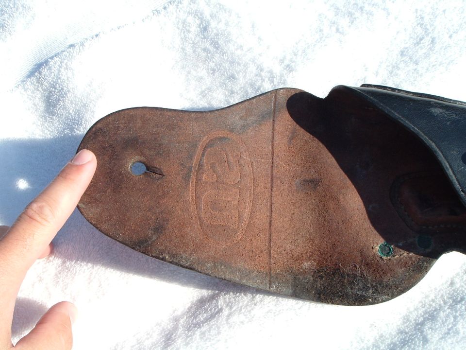 Leather part with embossed oval logo, finger pointing to hole