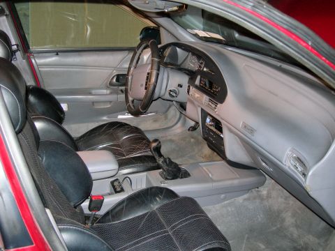 1992 Ford Taurus - Interior of a red Ford Taurus SHO shot through the open driver's door, showing gray dash with an SHO badge on the passenger side, black-and…