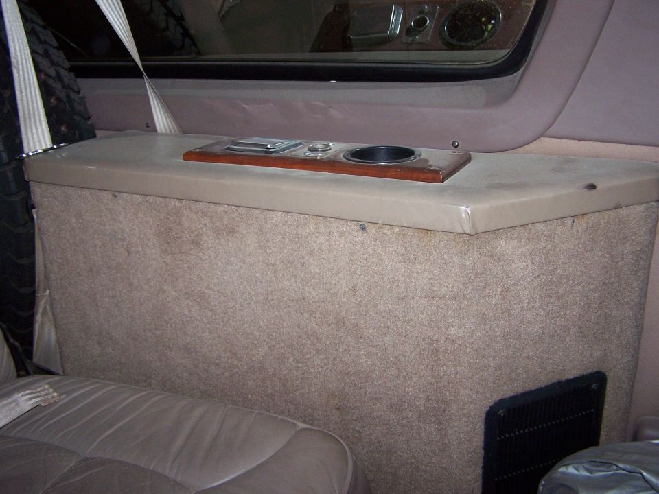 Tan carpeted rear bulkhead console with wood trim, ashtray and cupholder
