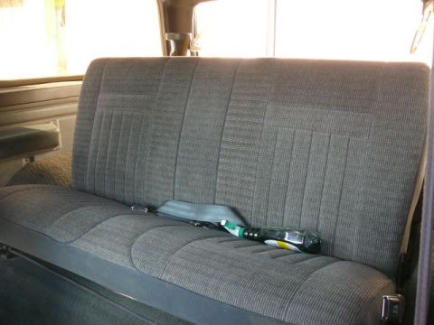 1988 Ford Bronco - The interior of a vehicle shows a rear bench seat with a seatbelt and a bottle resting on the cushion.