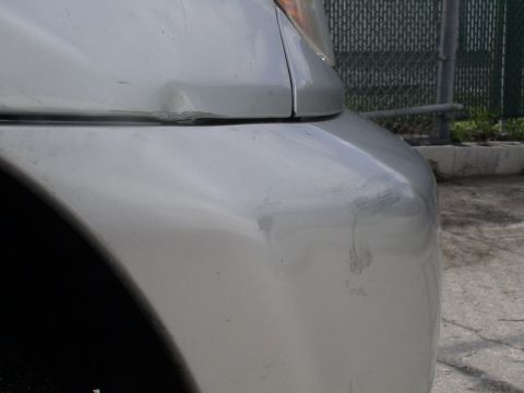 1993 Ford C-350 (Centurion Conversions) - Close-up of a silver car's front bumper and fender showing damage.