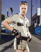 1996 Ford Bronco - A man dressed as a police officer, wearing short shorts and holding a handgun, stands in a street.