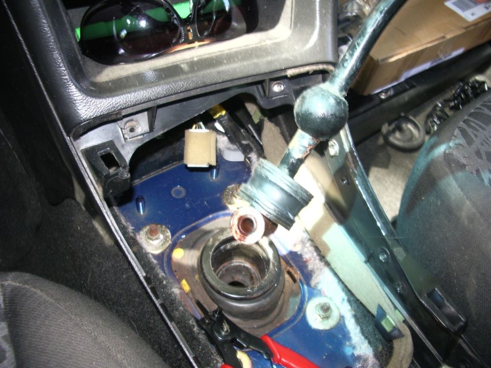 Disassembled gear shifter area in car interior, showing exposed parts and wiring