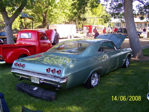 1972 Ford Ranchero - A teal coupe with distinctive quad taillights and chrome wheels is displayed on a grassy field, with a red pickup truck in the background.