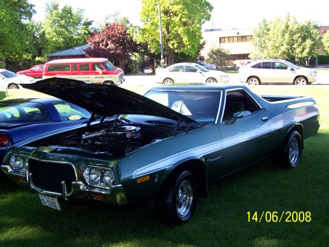 1972 Ford Ranchero - A green pickup truck with its hood open is parked on grass next to other vehicles.