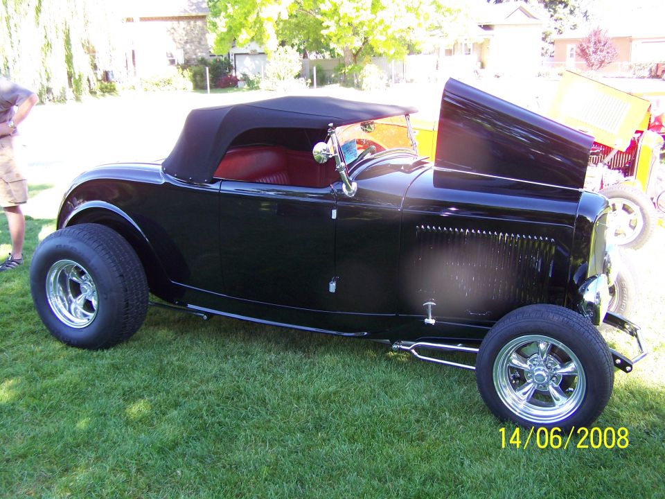 Black convertible hot rod with red interior and hood open. Another car is visible behind it