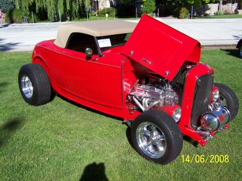 1972 Ford Ranchero - A red hot rod convertible with its hood up sits on a grassy lawn, displaying its engine.