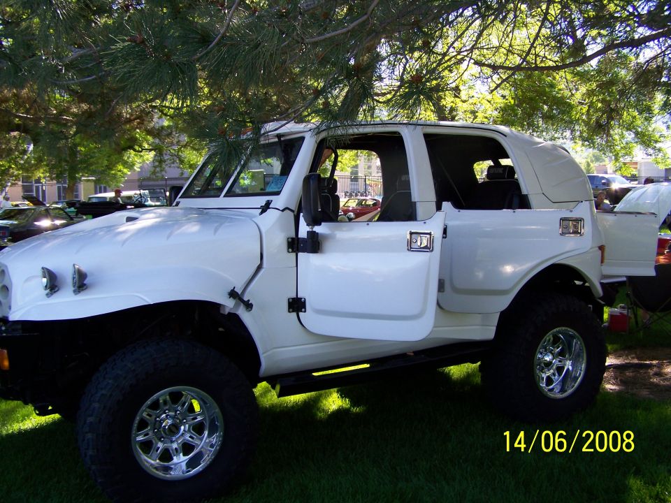 White custom SUV with doors open, parked on grass under trees. Date stamp in corner