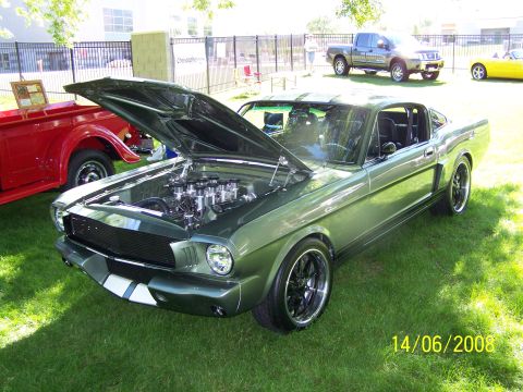 1972 Ford Ranchero - A green 1965 Ford Mustang Fastback is displayed with its hood open, revealing the engine, next to a red pickup truck.
