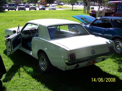 1972 Ford Ranchero - White 1965 Ford Mustang coupe with driver's door open, parked on grass next to a blue car.