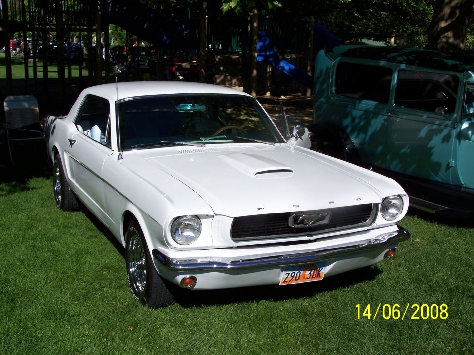 White 1965 Ford Mustang parked on grass, another vintage car behind it