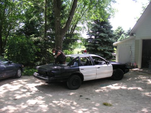 1997 Ford Crown Victoria - A two-tone black and white 1997 Ford Crown Victoria police car is parked outside a garage, with a person working on its roof.