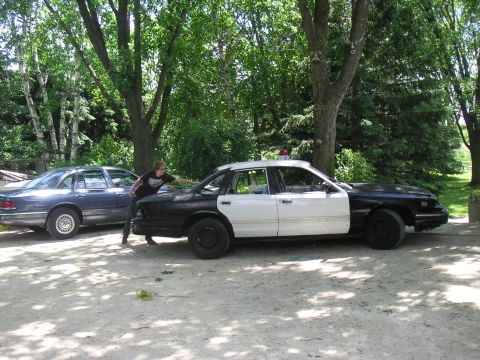 1997 Ford Crown Victoria - Two police cars are parked outdoors, with one person pushing the black and white car.