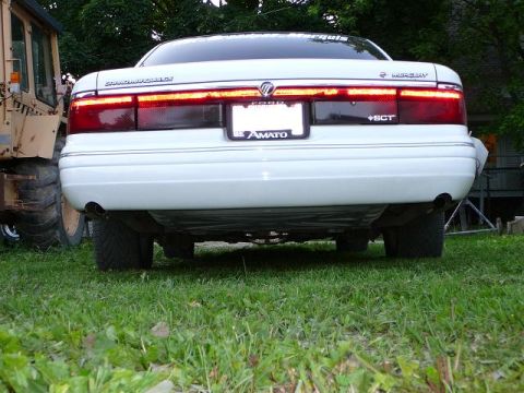 1997 Mercury Grand Marquis - The rear of a 1997 Mercury Grand Marquis is shown parked on grass next to a large yellow vehicle.