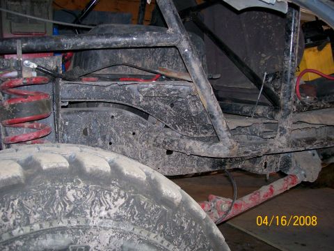 1984 Ford Bronco - The underside of a heavily modified off-road vehicle shows its suspension components and a muddy tire.