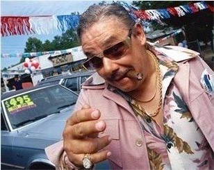 1969 Ford Torino - Man in a pink suit and sunglasses gestures while standing in front of cars at a dealership.