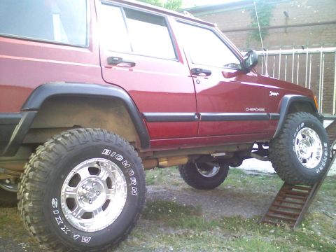 1998 Jeep Cherokee - This red Jeep Cherokee is positioned with its front tire on a ramp, its lifted suspension and off-road tires.