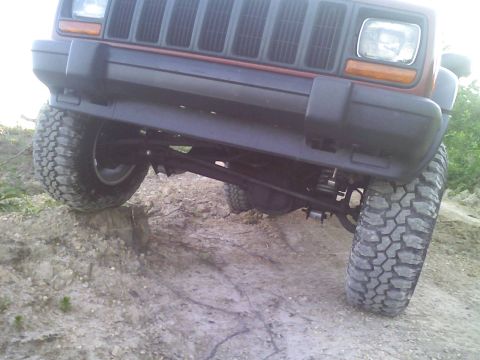 1998 Jeep Cherokee - A red Jeep Cherokee is shown from the front, angled upwards on a dirt incline, highlighting its off-road capabilities.