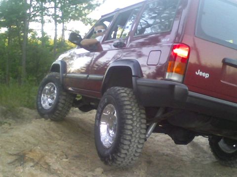 1998 Jeep Cherokee - This maroon 1998 Jeep Cherokee is shown off-roading on a dirt trail with its suspension lifted and equipped with large off-road tires.