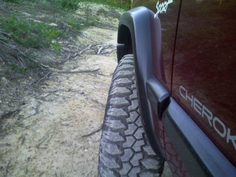 1998 Jeep Cherokee - Side view of a 1998 Jeep Cherokee on a dirt path, highlighting its off-road tire.